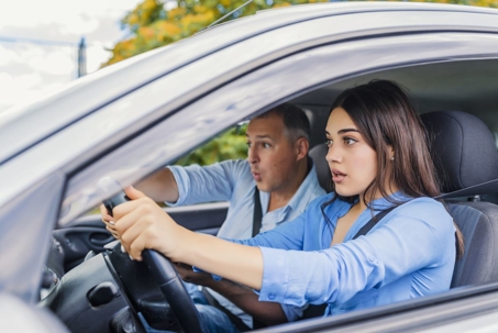 Young female driver looking worried while father gives direction